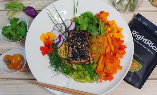 A beautiful presentation of a buddha bowl with rice, colorful vegetables and sesame tofu on a round white plate.
