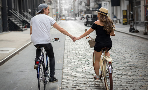 A couple holding hands while riding bicycles next to each other.
