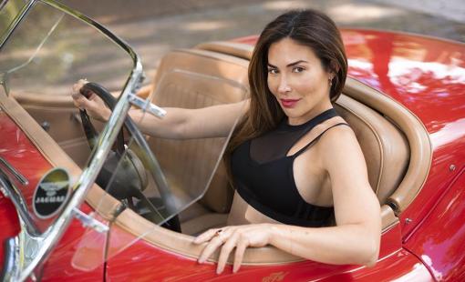 Bianca Jade is driving a Jaguar XK120 Roadster in a cherry red color with tan interior.