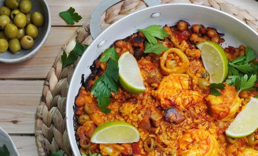 A spanish seafood paella ready to serve and made with green olives, shrimp, squid, parsley, rice and chicken sausage. 