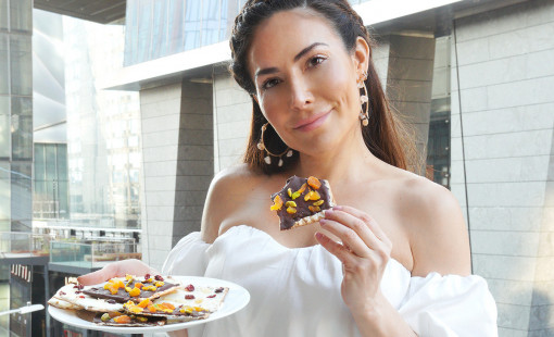 Bianca Jade holds her matzah bark recipe on a plate while about to take a bite of a piece of it. 